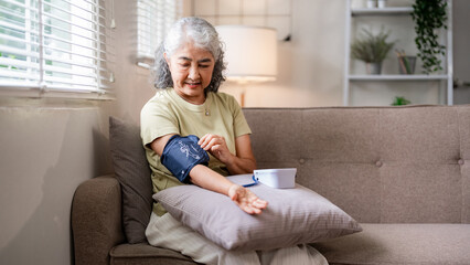 Asian older woman monitors blood pressure at home for self health wellness in living room setting...