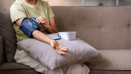Older Asian woman monitors blood pressure at home using medical device managing hypertension for heart health and wellness