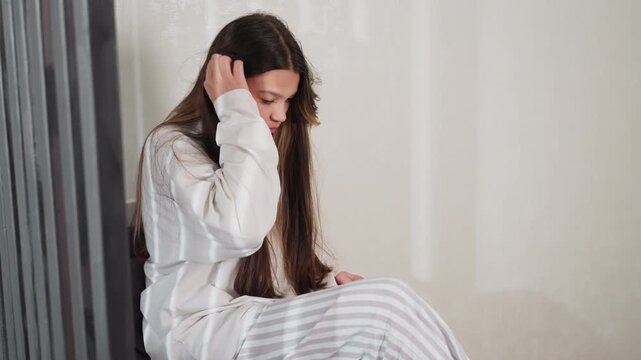 Young girl sits on chair in cozy room, lifts black nail polish bottle from side table then places it back, long hair loose, oversized light top, soft daylight mood, relaxed morning beauty moment