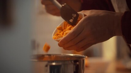 A person skillfully chops orange squash pieces with a knife, preparing ingredients for a hearty dish. The scene takes place in a cozy kitchen, filled with warm light, creating a homey atmosphere
