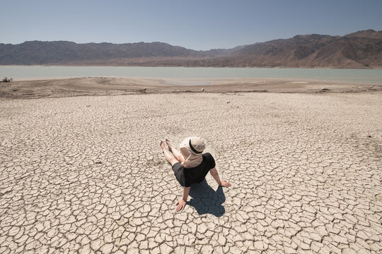 A woman sits on takyrs, cracks in the ground formed at the bottom of a dried-up lake or river in a deserted mountainous area.