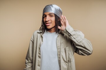 Young man wearing a headscarf listens intently while posing against a beige background in a casual setting