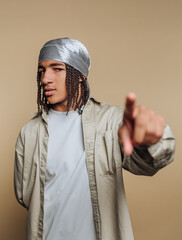 Young man with braids and gray bandana poses confidently against a plain background