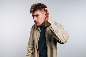 Young man listening closely in a neutral setting, showing curiosity and engagement with surroundings