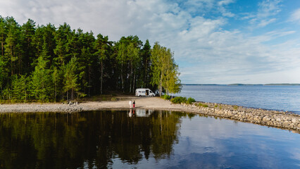 A serene scene unfolds at Lake Saimaa in Finland, featuring a couple enjoying the peaceful shore. Lush green trees frame the clear water, inviting moments of relaxation and connection with nature.