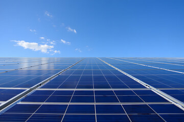 Vast expanse of blue solar panels stretching towards a clear sky with scattered white clouds