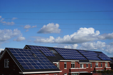 Fototapeta premium Modern brick houses with solar panels installed on the roof under a blue sky with clouds