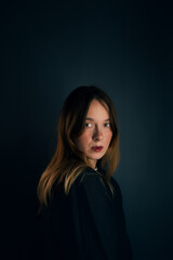 Fototapeta premium Serious and Intentional Studio Portrait of a Woman. The scene is lit with warm, soft lighting that separates her from the dark, moody background, highlighting her natural expression and hair color.