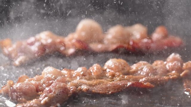 Camera follows cooking bacon on grill. Shot with high speed camera, slow Motion.