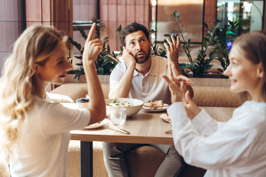 Man feeling annoyed by arguing women at restaurant table
