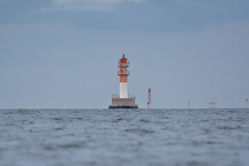 Red and white striped navigation beacon in the middle of the  Szczecin Lagoon under blue sky.	