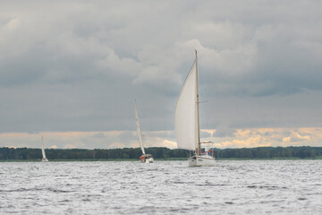 Obraz premium Sailboats gliding across the Szczecin Lagoon in Poland under a dramatic cloudy sky