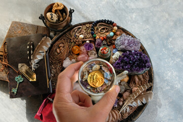 Magic crystal ball in hand, witch altar with amulets, gemstones, spell books, cauldron, witchery stuff on table. Crystal Magic. esoteric ceremony, spiritual ritual for relax, meditation. top view