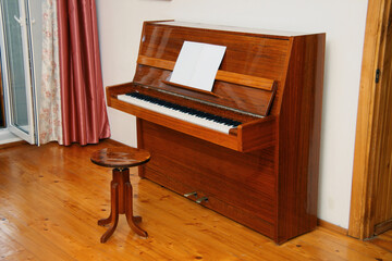 Elegant wooden upright piano with sheet music and a matching stool in a sunlit room
