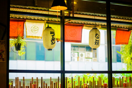 Experience the vibrant ambiance of a Japanese eatery, featuring traditional ramen and takoyaki lanterns hanging gracefully by a sunlit window, inviting diners into an authentic culinary journey.