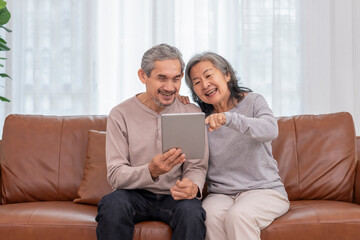 happy senior married couple enjoy surfing internet online on tablet computer in a cozy room together at home