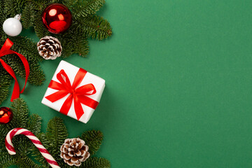 Festive Christmas tree branches with gift box on color background, top view