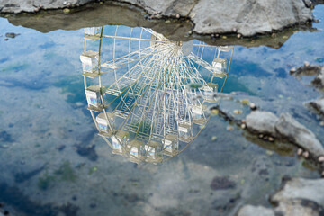 A seaside ferris wheel reflected in a blurred rock pool, blending coastal textures with playful...