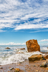 Vertical shot of a fallen rock fragment against the backdrop of rolling surf, the pristine power and beauty of the elements, texture for product design with the natural authenticity of the sea