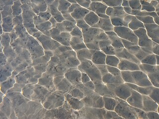 Clear water ripples on sandy bottom create mesmerizing patterns under sunlight in a tranquil environment