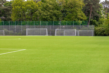 Quiet Empty Soccer Field With Three Goals Surrounded By A Fence And A Line Of Green Trees