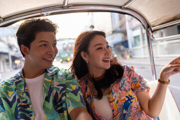 Young Asian couple tourist traveling on local Tuk Tuk Taxi exploring the city in Road in Bangkok Thailand during a holiday