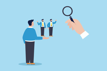 Hand holding magnifying glass examines two small business people presented by a larger figure