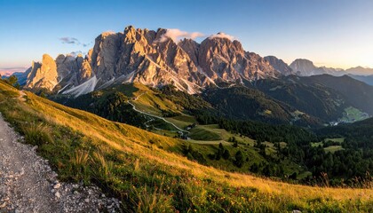 Mountain vista at sunset, with a winding trail.  Rocky peaks, bathed in golden light, rise above a valley carpeted with meadows and forests.  A path descends into the valley below
