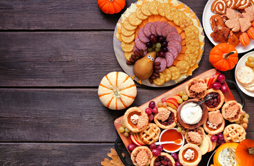 Thanksgiving appetizers, sweets and grazing boards. Top down view side border on a dark wood background. Pumpkin and apple snacks, pies, turkey cheese platter, desserts.