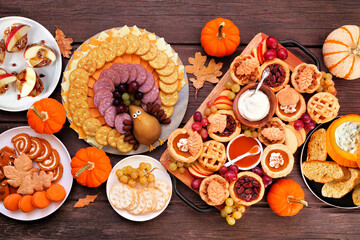 Thanksgiving appetizers, sweets and grazing boards. Top view table scene on a dark wood background. Pumpkin and apple snacks, pies, turkey cheese platter, desserts.