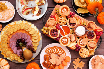 Thanksgiving appetizers, sweets and grazing boards. Overhead view table scene on a dark wood background. Pumpkin and apple snacks, pies, turkey cheese platter, desserts.
