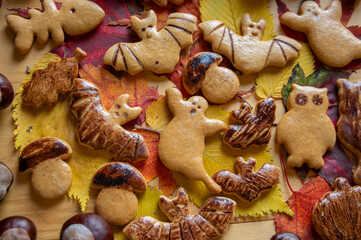 Decorated gingerbread cookies for Halloween celebration spread on table with colorful autumnal leaves and chestnut fruit
