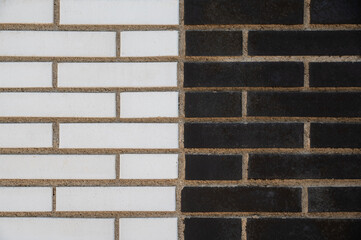 Fragment of a wall divided into two sections: one with light tiles, the other with dark ones. The grout is visible between them. Suitable for use as an abstract background and texture.