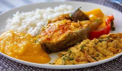 Traditional Brazilian fish moqueca with fresh yellow hake fish fillets, Cynoscion acoupa, with farofa, pirão and white rice. Pescada amarela and dende oil.