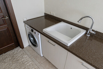 A functional laundry area with a washing machine, sink, dark countertop, and cabinet in a clean, modern style