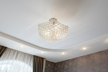 A low-angle shot showcases a modern ceiling with a crystal chandelier, recessed lights, decorative...