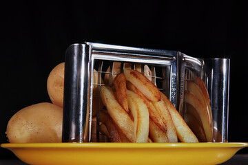 Raw and fried potatoes on a yellow plate. Black background
