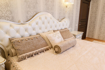 Elegant bedroom featuring a tufted white headboard, decorative pillows, and ornate wallpaper. A...