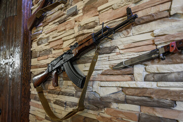 An AK-47 assault rifle is mounted on a textured stone wall, alongside a bayonet