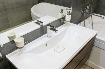 Modern bathroom detail: white sink, chrome faucet, grey tile, and a mirrored surface