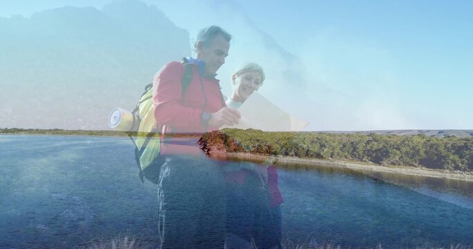 Mature couple consulting map at lakeshore, wearing hiking clothes, yellow backpack and rolled mat - Powered by Adobe