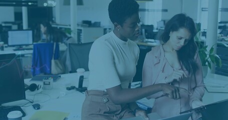 Pointing at laptop, woman in white top collaborating with colleague wearing pink blazer at office