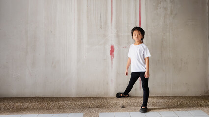 Portrait of cute Asian child in a simple white t-shirt and black leggings, standing. Background is...