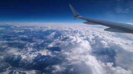 Obraz premium Aerial view of snow capped mountains and fluffy clouds from an airplane window