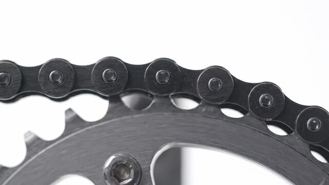 Detailed shot of a bicycle chain in motion as it rotates around a metal chainring, a crucial part of the bike's drivetrain. This isolated mechanism is showcased against a clean white backdrop