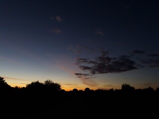 Sunset horizon with dark trees and bright orange sky fading into deep blue.