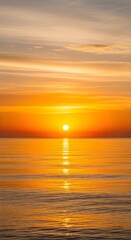 Brilliant orange sunset over calm water with reflection wispy clouds in the sky