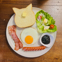 Top view of breakfast set with sausage, bacon, fried egg, cat-shaped bread with butter, blueberry jam, and salad on wooden table. Perfect for food blogs and menus.
