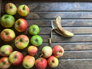 Close up of ripe red and green apples on a  clear wooden table background the fruit freshly harvest organic allotment orchard garden in Summer interior flat top view with copy space and banana skin