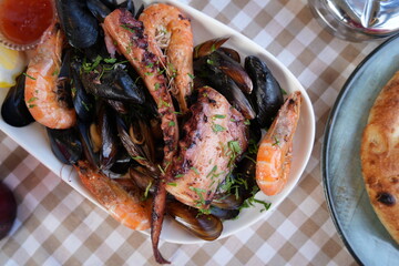 Seafood platter with shrimp, mussels, and octopus served in a restaurant. Fresh Mediterranean cuisine with grilled seafood and herbs on a checkered tablecloth.